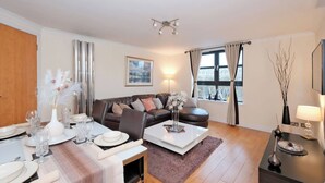 A modern living room with a sofa, coffee table, and dining area set up for a meal. - Executive 2Bed City Centre Apartment in Aberdeen (Aberdeen)