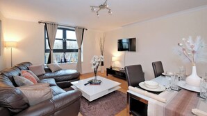 A modern living room with a leather sofa, a white coffee table, a dining table set for two, and a flat-screen TV mounted on the wall. - Executive 2Bed City Centre Apartment in Aberdeen (Aberdeen)