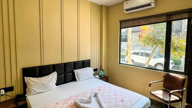 Hotellihuone, jossa on sänky, tuoli, ikkuna, josta on näkymä ulos, ja ilmastointilaite.