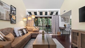 Ein modernes Wohnzimmer mit einem braunen Ledersofa, einem Holztisch und einem großen Fenster mit Blick auf einen Balkon.