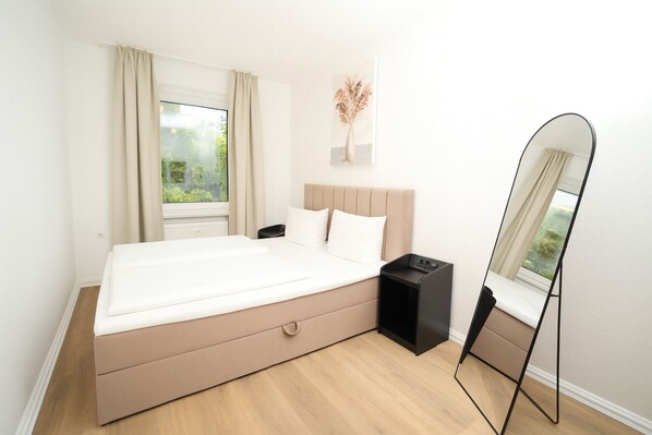 A modern bedroom with a large bed, a bedside table, a nightstand, a mirror, and a window with curtains.