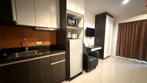 Eine moderne Küche mit dunklen Holzschränken, einer Edelstahl-Spüle und einem eingebauten Ofen. Ein kleiner Sitzbereich mit einem Stuhl und einem an der Wand montierten Flachbildfernseher. Der Raum hat einen Fliesenboden und einen braunen Vorhang am Fenster.