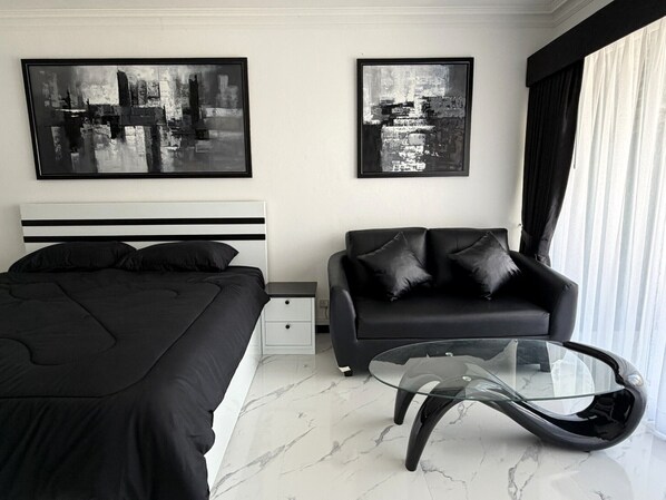 Une chambre à coucher moderne avec un lit, un canapé, une table basse en verre et deux tableaux abstraits accrochés au mur.