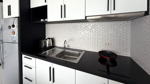 Een moderne keuken met witte kastjes, een zwart aanrecht, een roestvrijstalen spoelbak en een rode pan.
