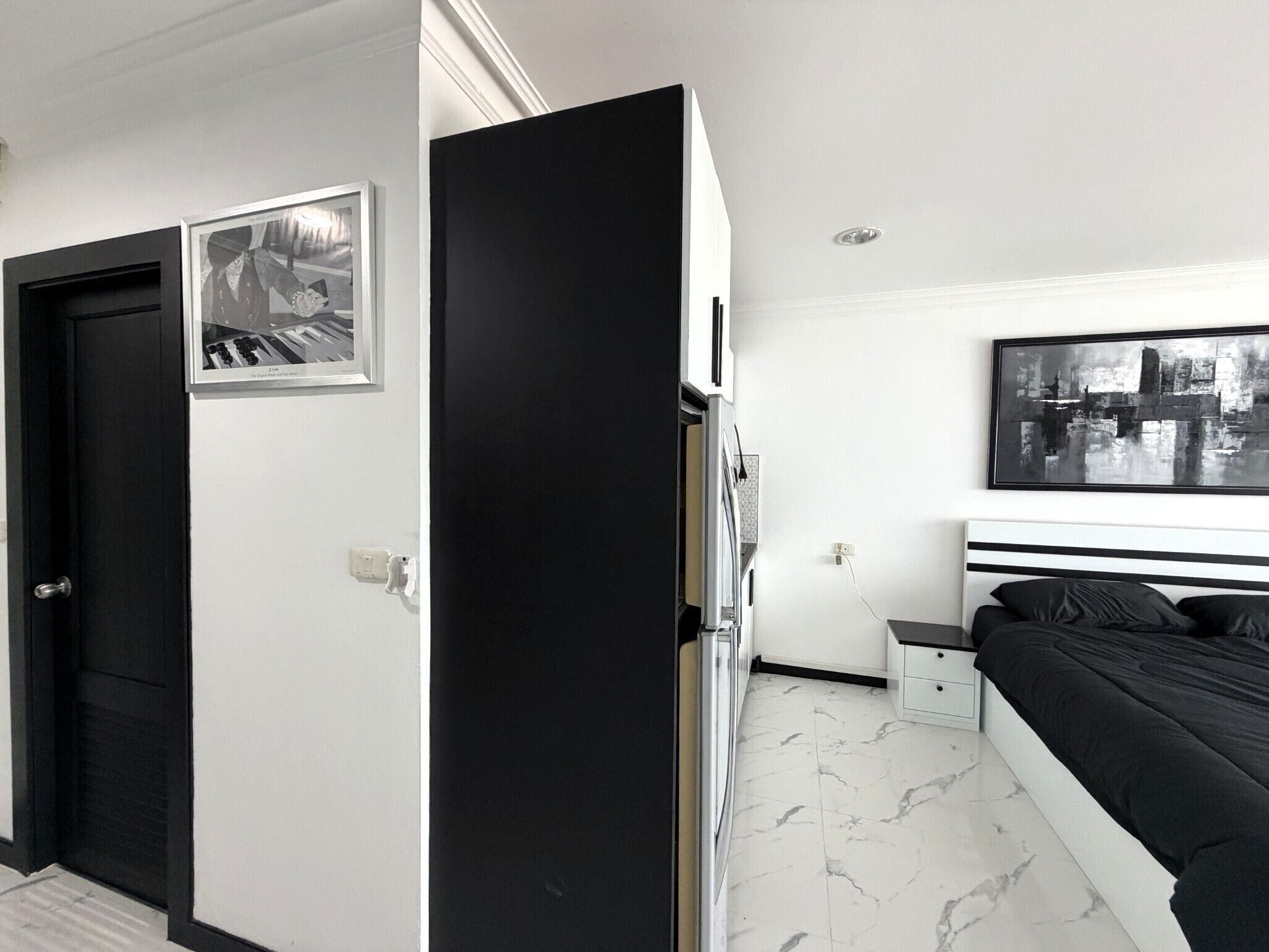A modern bedroom with a bed, a nightstand, a wall-mounted TV, and a door.