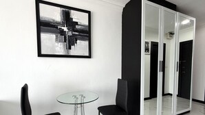 Een moderne kamer met een glazen tafel, twee zwarte stoelen, een zwart-wit abstract schilderij en een grote spiegel met een zwarte lijst.