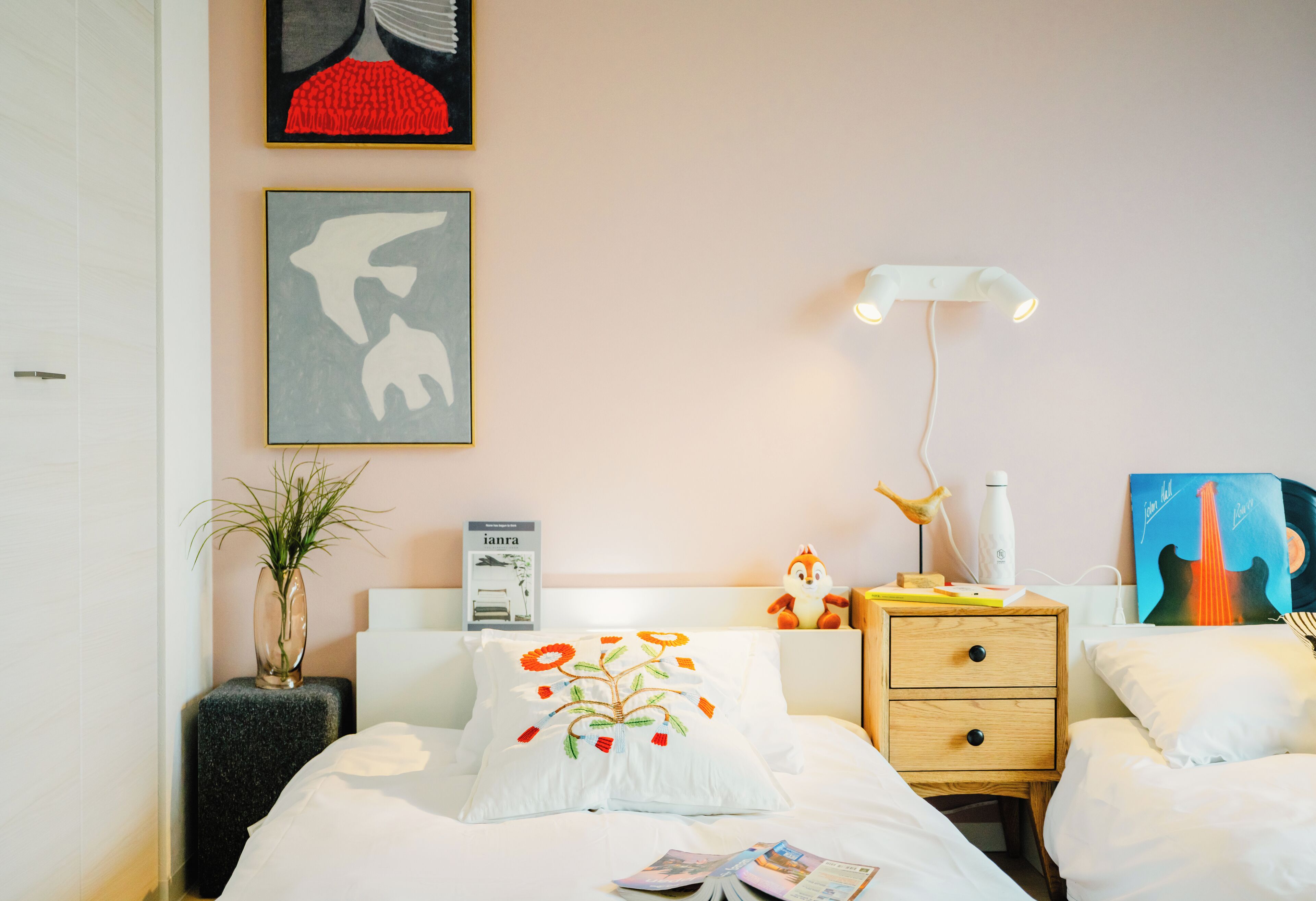 Ein Hotelzimmer mit Bett, Nachttischen, einer Lampe, einer Pflanze und Kunstwerken an den Wänden.
