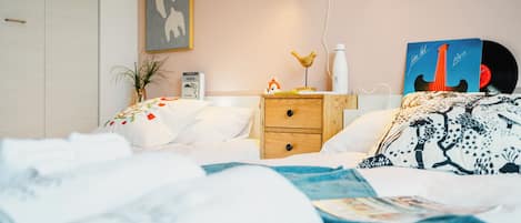A neatly made bed with a blue and white patterned blanket, a bedside table with a lamp, a framed picture, and a small plant.