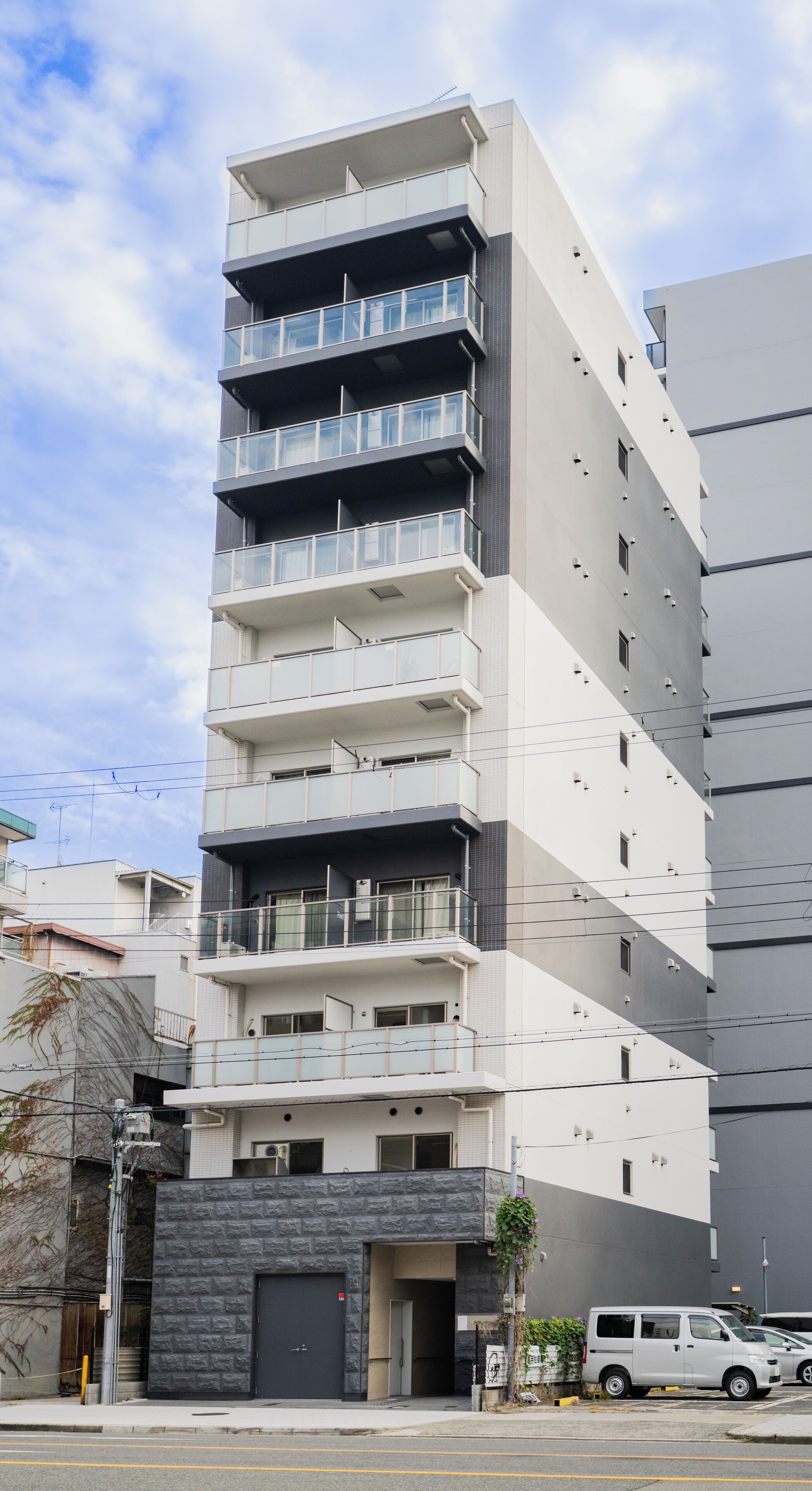 A multi-story residential building with balconies, a garage, and a parked van.