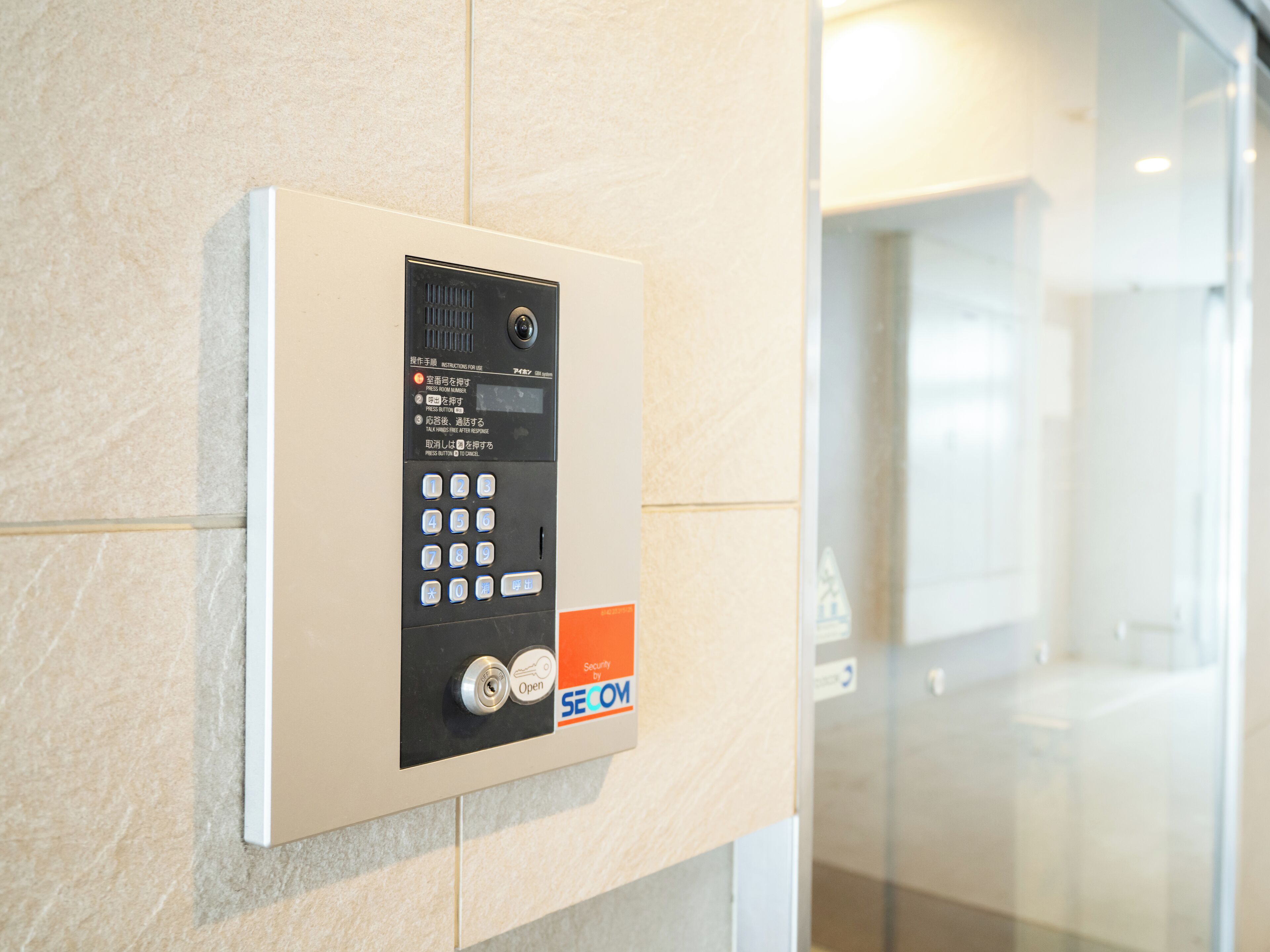 A wall-mounted security keypad with instructions in multiple languages, a keyhole, and a "SECURITIES BY SECOM" label.