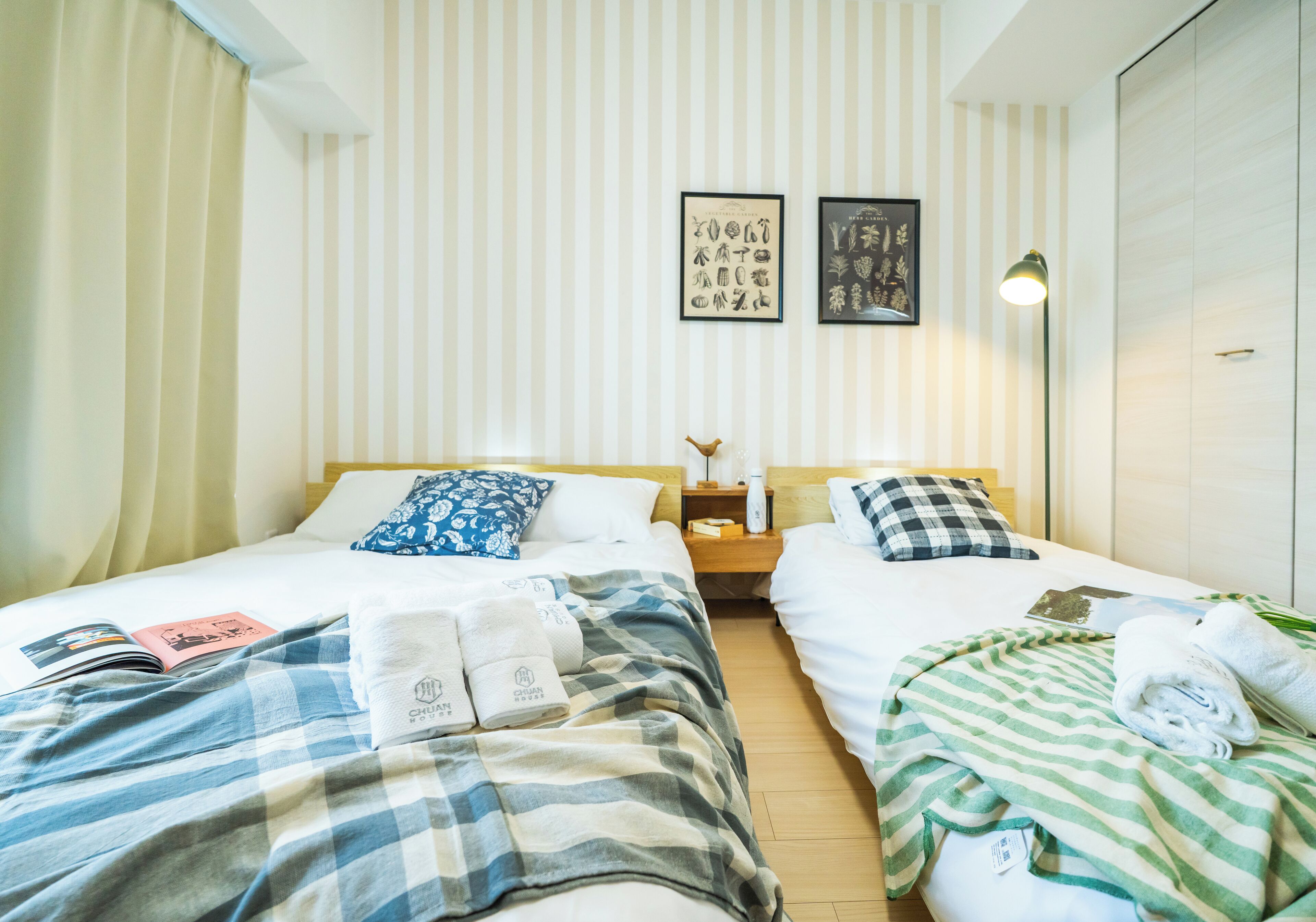 A hotel room with two beds, striped curtains, a nightstand with a lamp, and artwork on the wall.