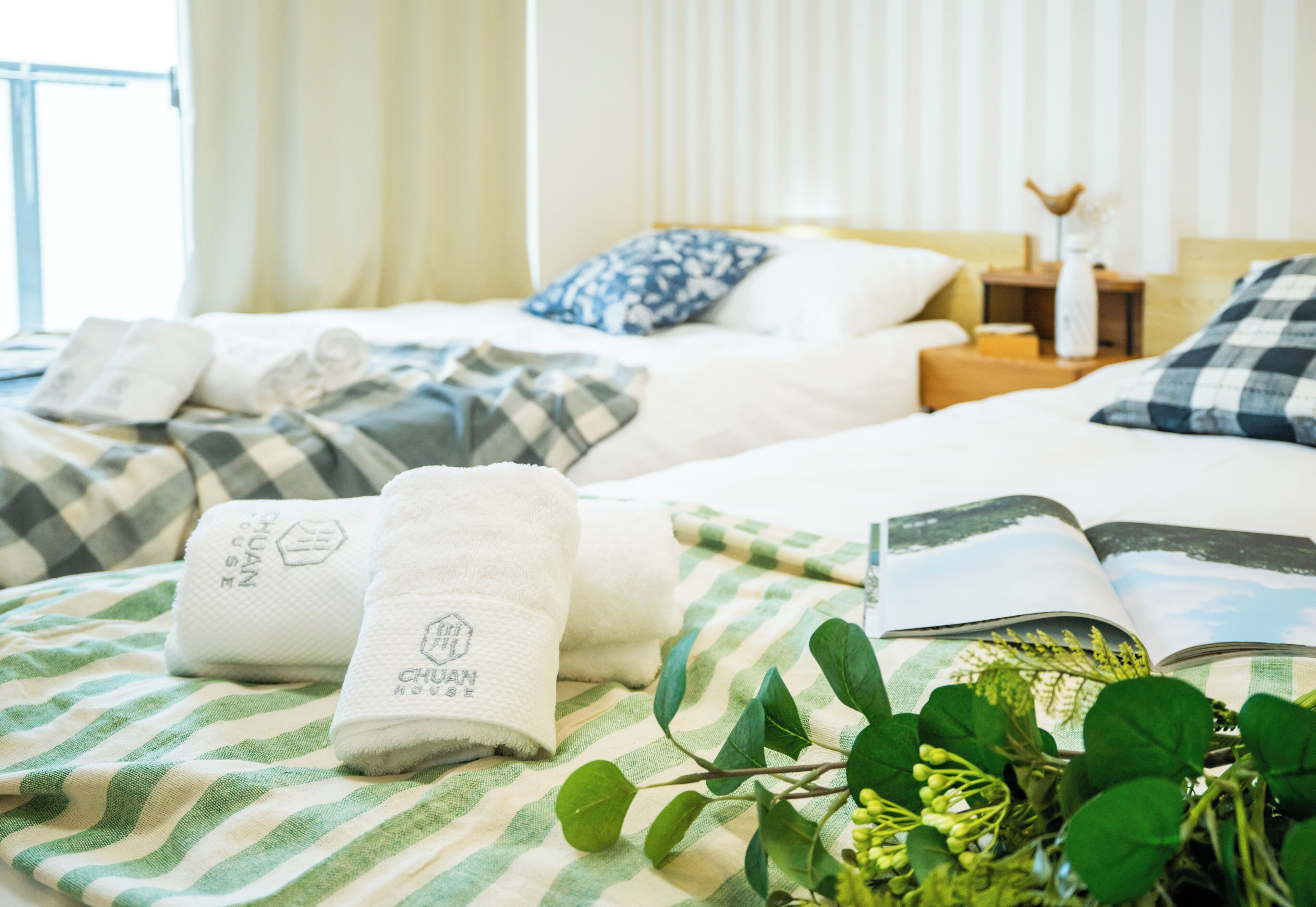 A hotel room with two beds, green and white striped bedding, a book, and a vase with green plants.