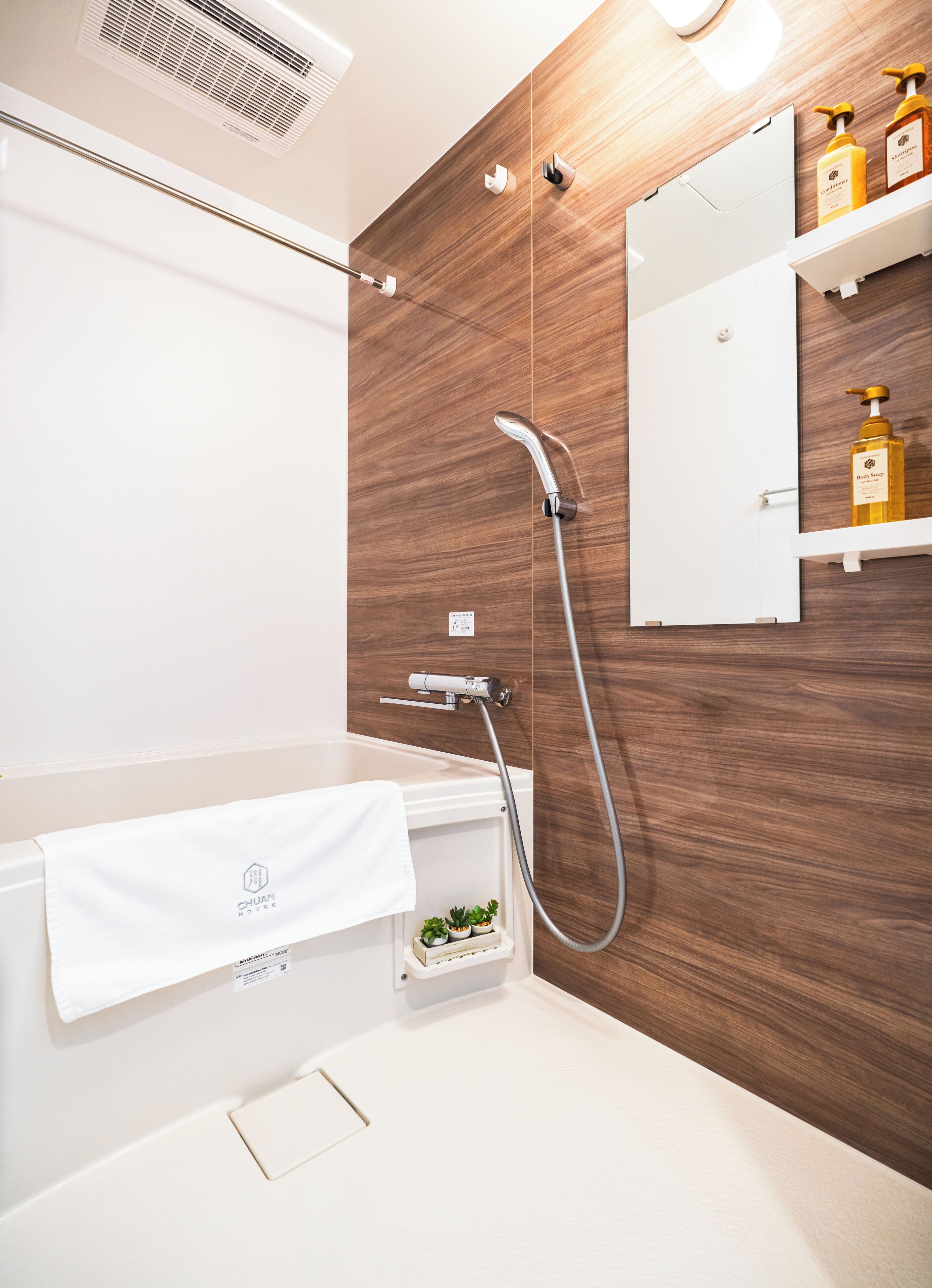 Et moderne badeværelse med trævæg, et hvidt badekar, brusehoved, et håndklædetørrestativ og en hylde med toiletartikler.