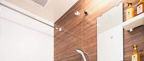 Ein modernes Badezimmer mit einer Holzwand, einer weißen Badewanne, einer Handbrause, einem Handtuchhalter und einem Ablagefach mit Pflegeprodukten.