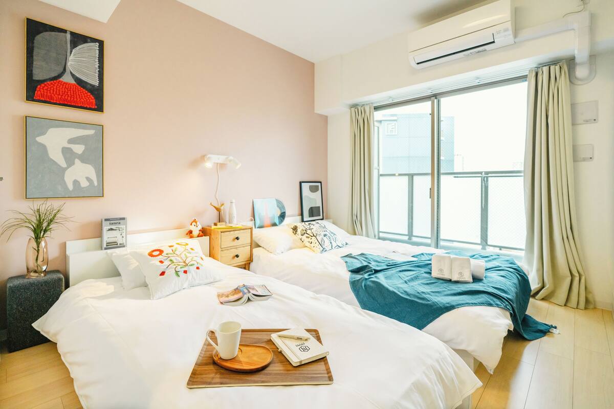 Une chambre d’hôtel moderne avec deux lits, une grande fenêtre avec des rideaux, un appareil de climatisation et des œuvres d’art accrochées aux murs.