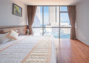 A modern hotel room with a large bed, a view of a cityscape, and a balcony with a pool. - Holiday Central Nha Trang (Nha Trang)