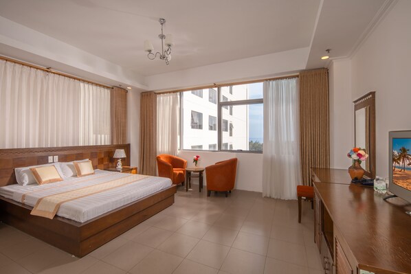 A hotel room with a large bed, two chairs, a small table, a TV, and a window with curtains. - Holiday Central Nha Trang (Nha Trang)