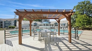 A covered outdoor area with a pool, seating, and a view of residential buildings in the background. - New Convenient Getaway near USC & Riverwalk Trails (Cayce)