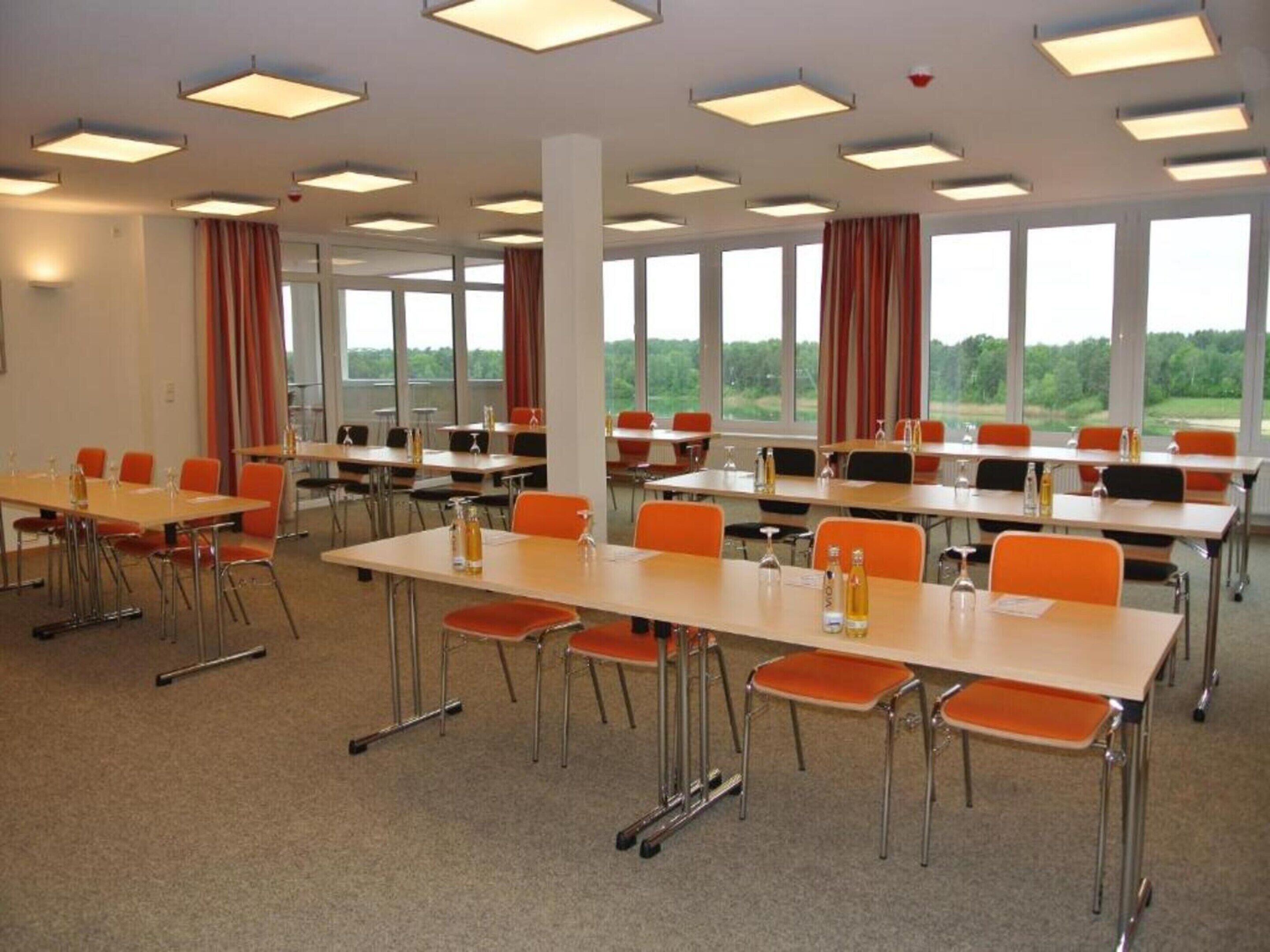 A conference room with multiple tables and chairs, large windows, and ceiling lights.