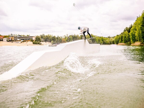 A person riding a wakeboard on a ramp by a body of water with buildings in the background. - Bernsteinsee Hotel and Ferien Superior Suite (Sassenburg)