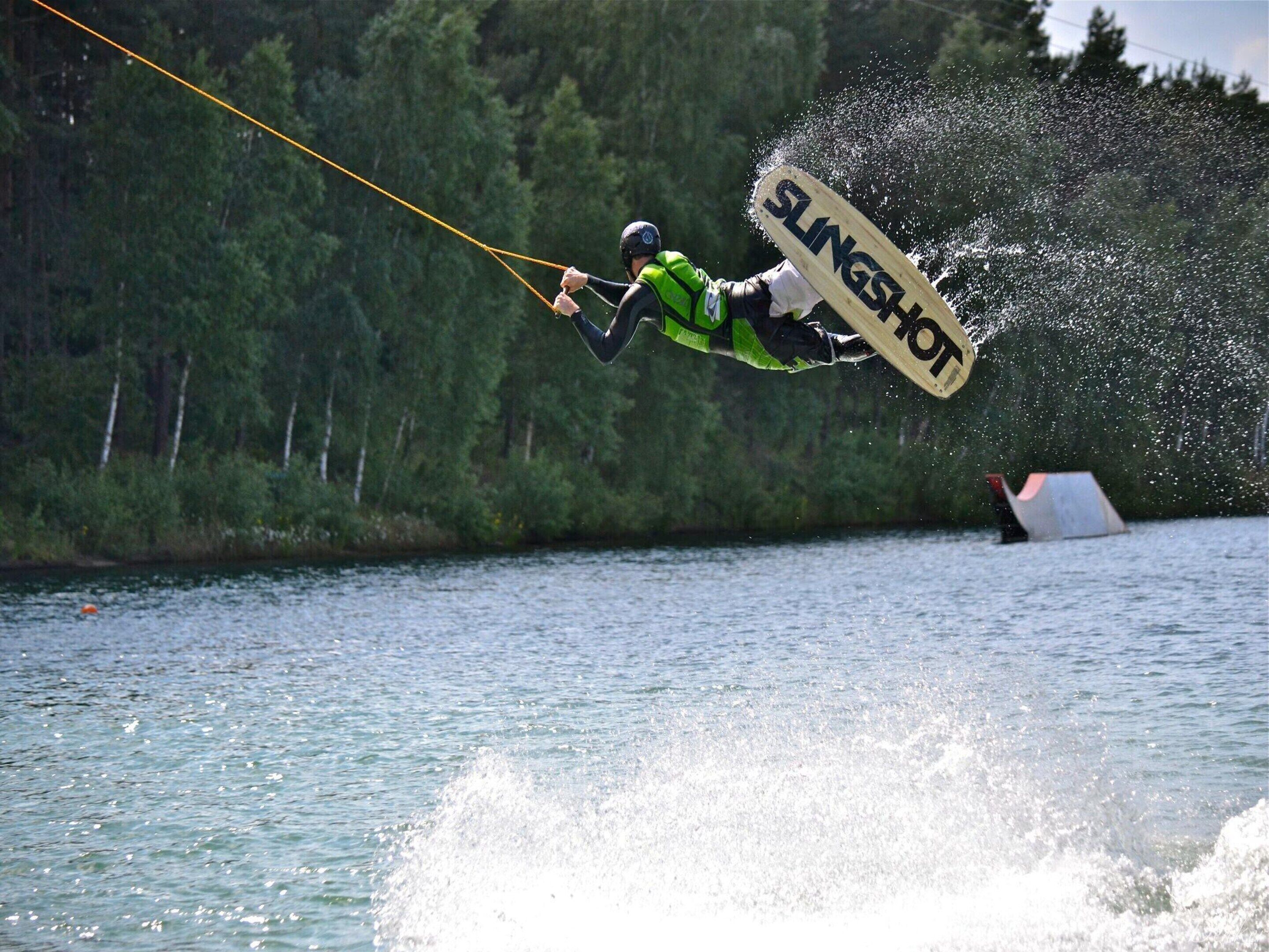 Un pratiquant de wakeboard en plein saut, avec de l’eau qui éclabousse tout autour.