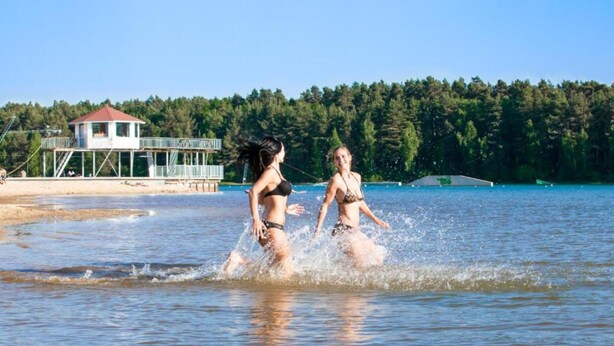 Two people in a swimming pool with a building and trees in the background. - Bernsteinsee Hotel and Ferien Superior Suite (Sassenburg)