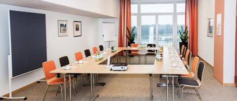 Une salle de conférence avec une longue table, des chaises, un tableau blanc et de grandes fenêtres équipées de rideaux.