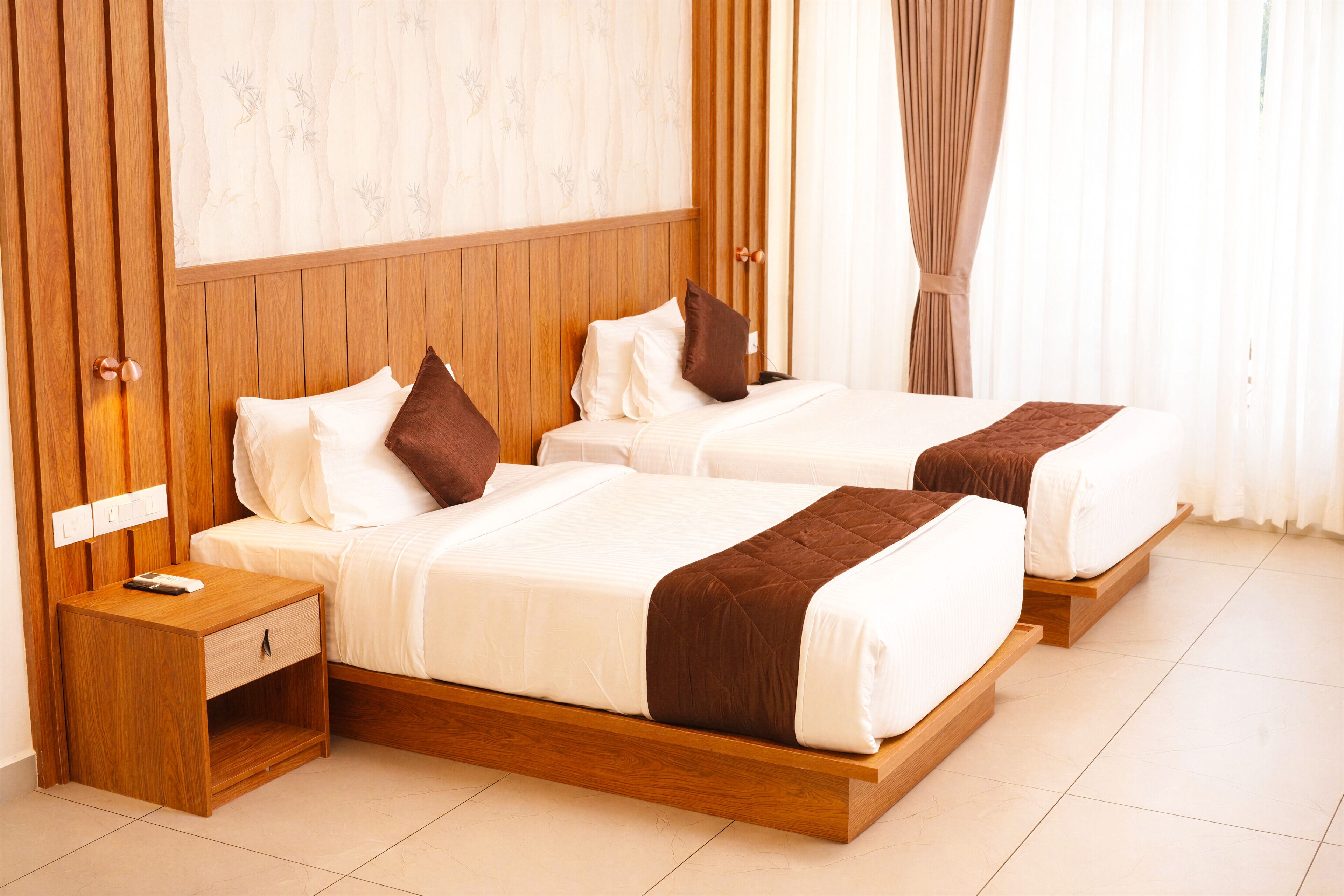 A hotel room with two beds, wooden headboards, a nightstand, and a wall-mounted light.