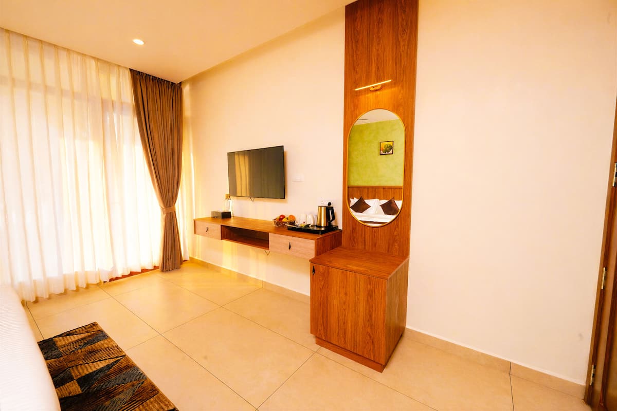 Een hotelkamer met een bed, een televisie, een houten kast, een spiegel en een raam met gordijnen.