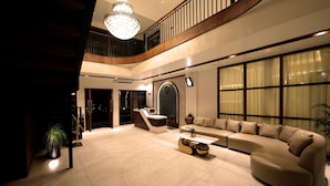 A spacious living area with a high ceiling, a chandelier, a reception desk, and a large window with curtains. - Malankara palace lake view resort & spa (Thodupuzha)