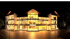 A multi-story hotel with a central atrium, balconies, and a well-lit facade. - Malankara palace lake view resort & spa (Thodupuzha)