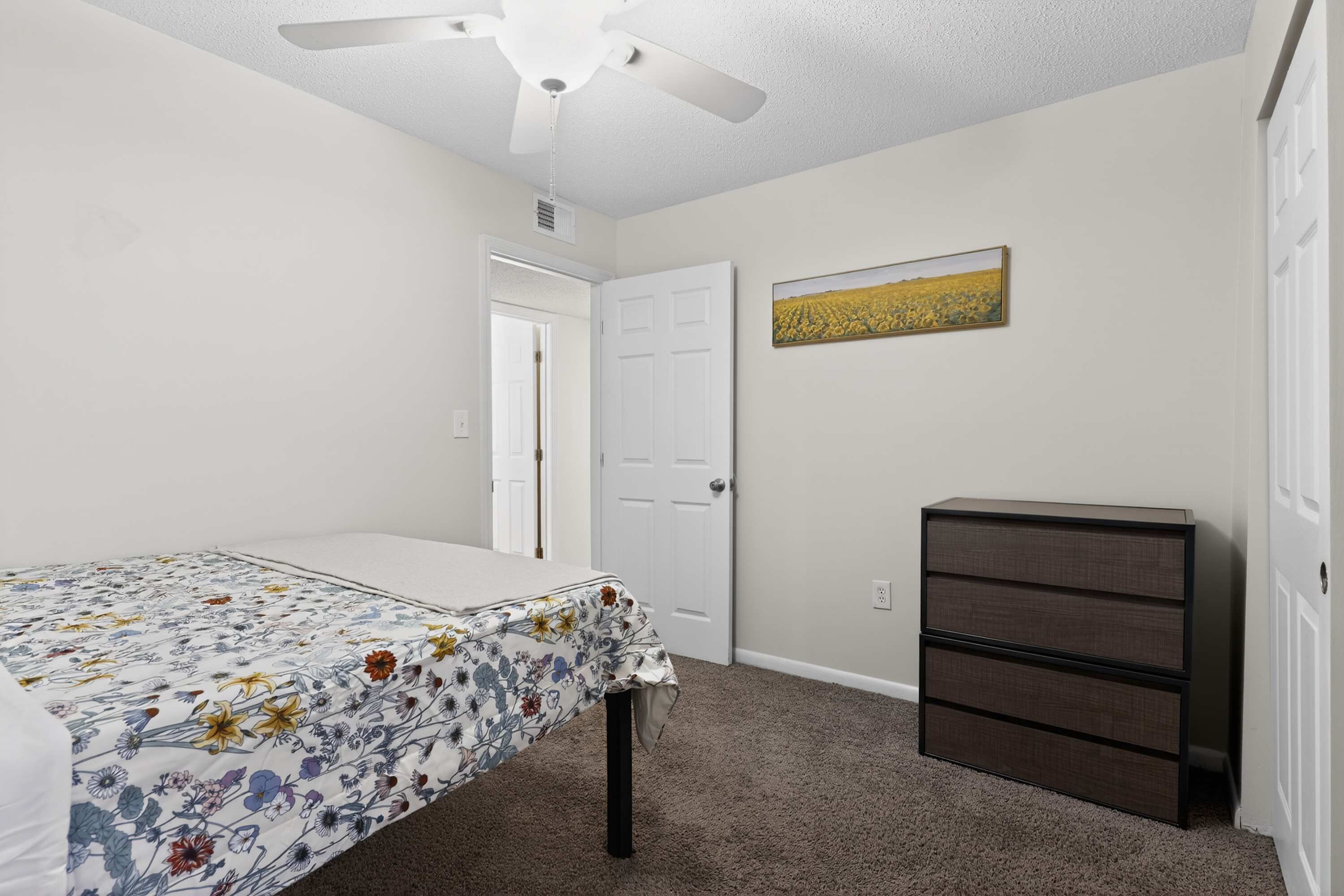 A bedroom with a bed, a dresser, a ceiling fan, and a door.