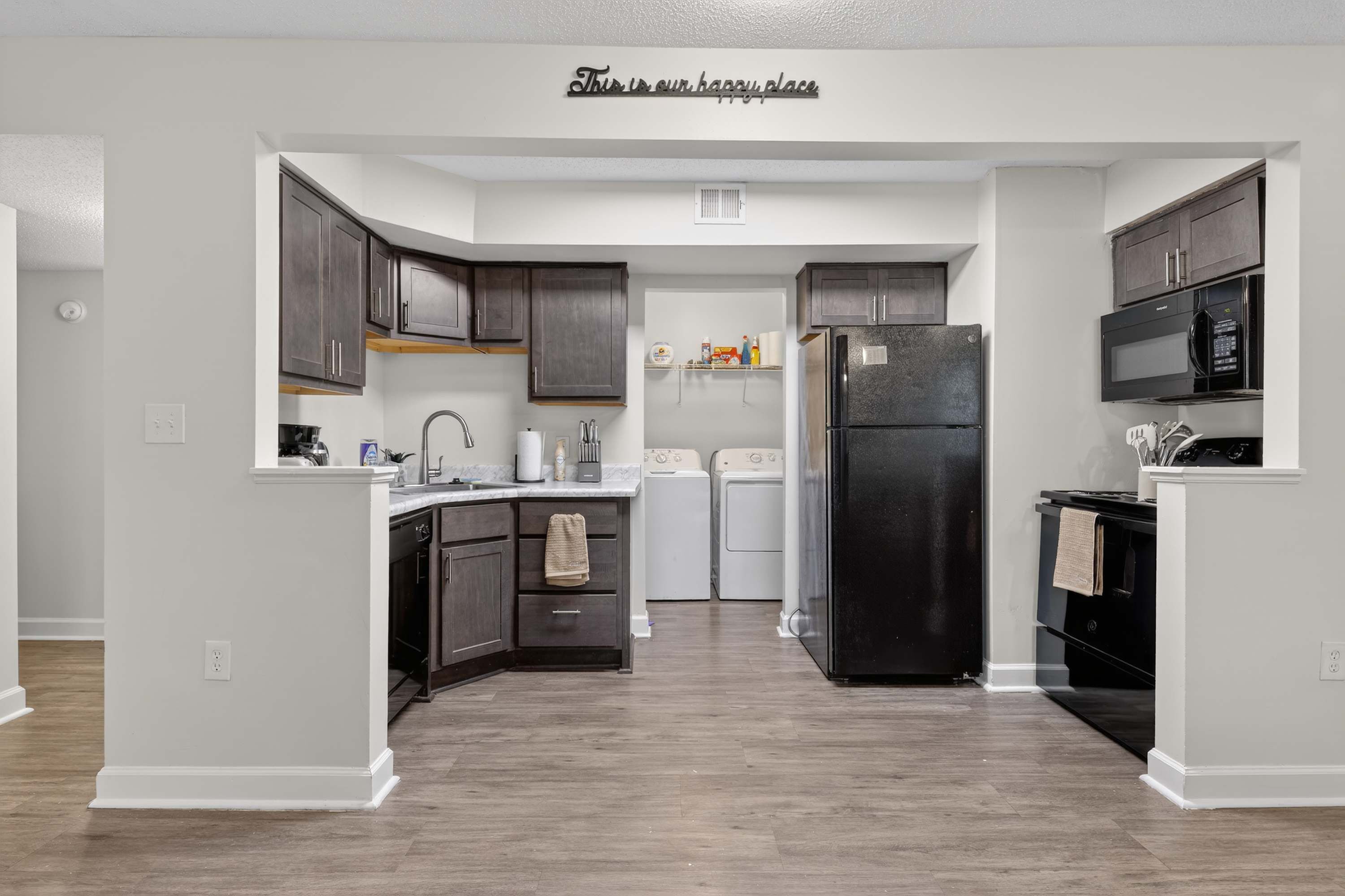 A modern kitchen with dark wood cabinets, a black refrigerator, and a microwave.