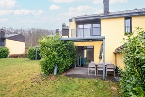 A yellow building with a covered patio, a small garden, and a clear sky. - Nature retreat home in Hambachtal Holiday Park (Oberhambach)