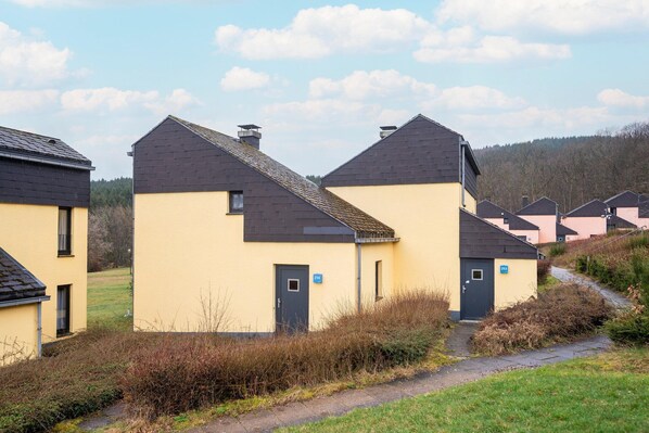 A row of yellow buildings with dark roofs, numbered 313 and 314, surrounded by greenery and a clear sky. - Nature retreat home in Hambachtal Holiday Park (Oberhambach)