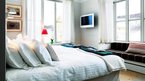 Een slaapkamer met een bed, een aan de muur bevestigde televisie en grote ramen voorzien van gordijnen.