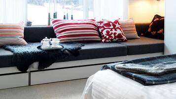 A cozy room with a sofa bed, a window with curtains, a bedside table with a lamp, and a view of the outdoors.