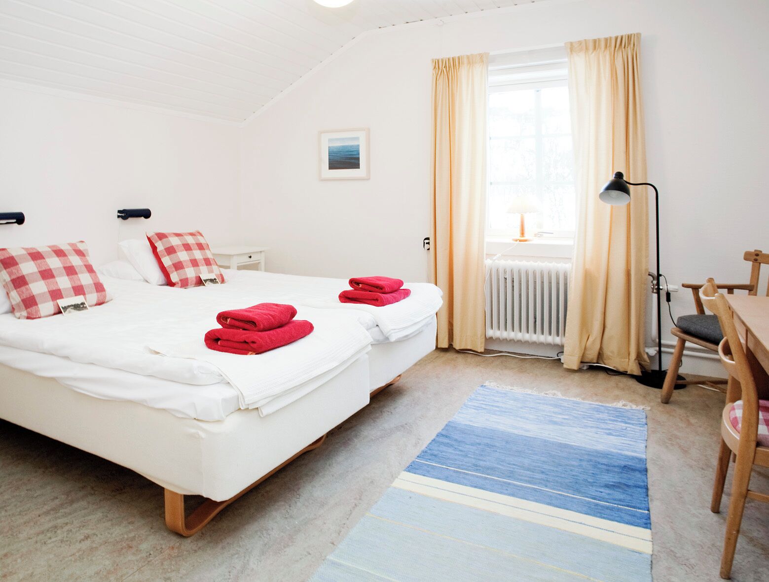 A bedroom with two beds, a desk, a chair, a lamp, and a window with curtains.