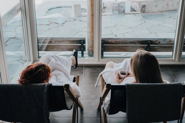 Two people seated in chairs facing a large window with a view of a tiled patio area. - Fjällnäs Est. 1882 (Tänndalen)