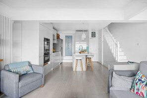 Una cocina moderna con armarios blancos, una isla central y una escalera que conduce a otro nivel.