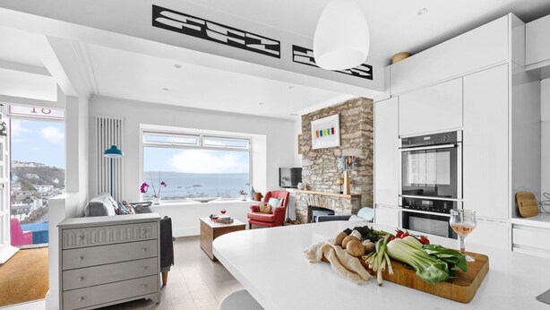 Une cuisine moderne dotée d’un grand îlot central, de meubles blancs et d’un mur d’accent en pierre.