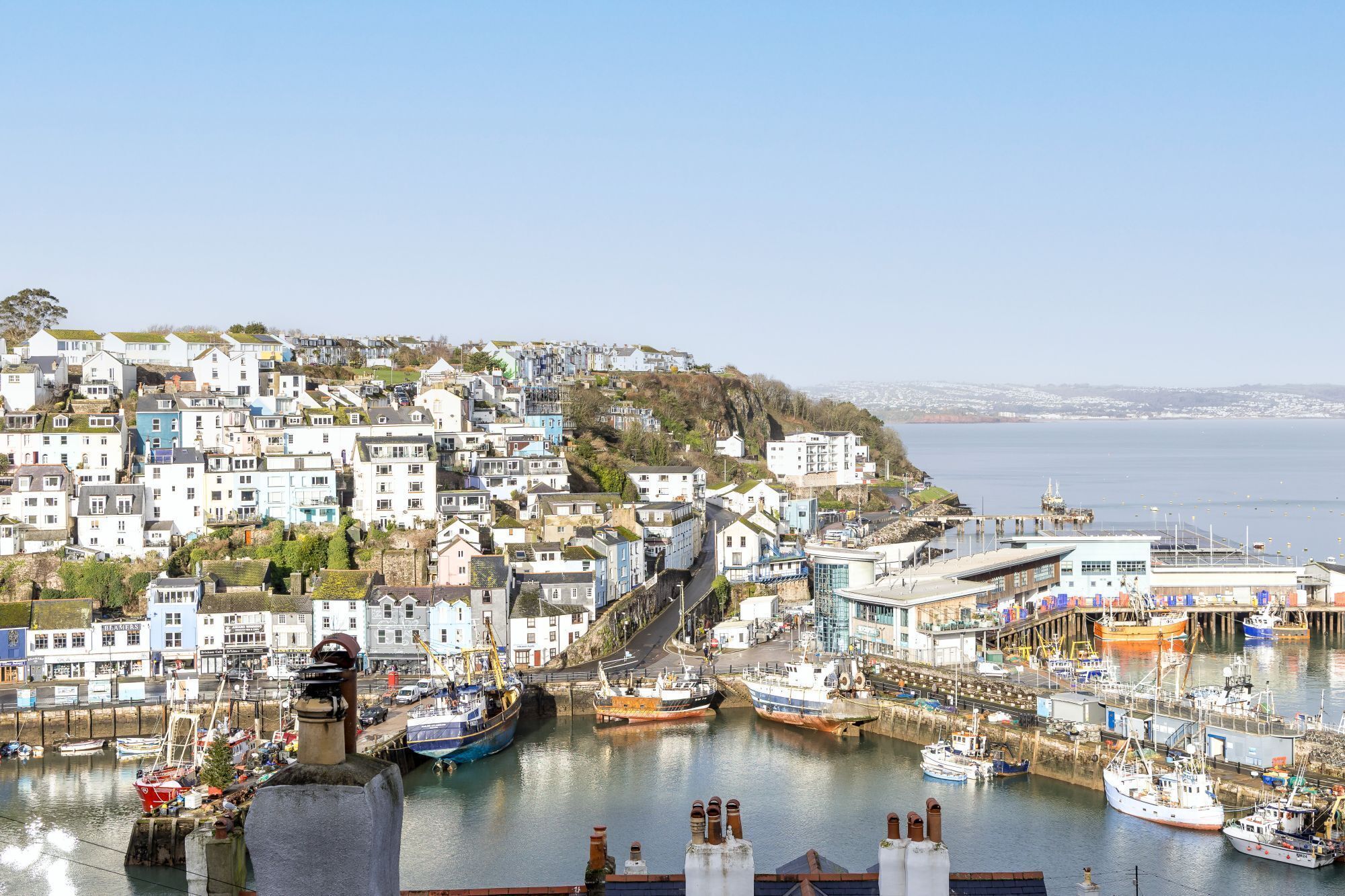 A coastal town with a harbor filled with boats, buildings with balconies, and a clear view of the sea.