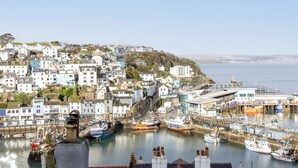 Une ville côtière dotée d’un port rempli de bateaux, de bâtiments avec des balcons et offrant une vue dégagée sur la mer.