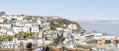 A coastal town with a harbor filled with boats, buildings with balconies, and a clear view of the sea.
