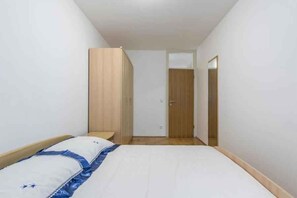 Habitación de hotel pequeña y estrecha, con una cama, un armario de madera y una puerta que da a otra habitación.