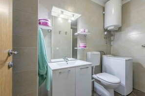 Un baño moderno con lavamanos, espejo y retrete blancos. Hay dos estantes rosados encima del espejo.