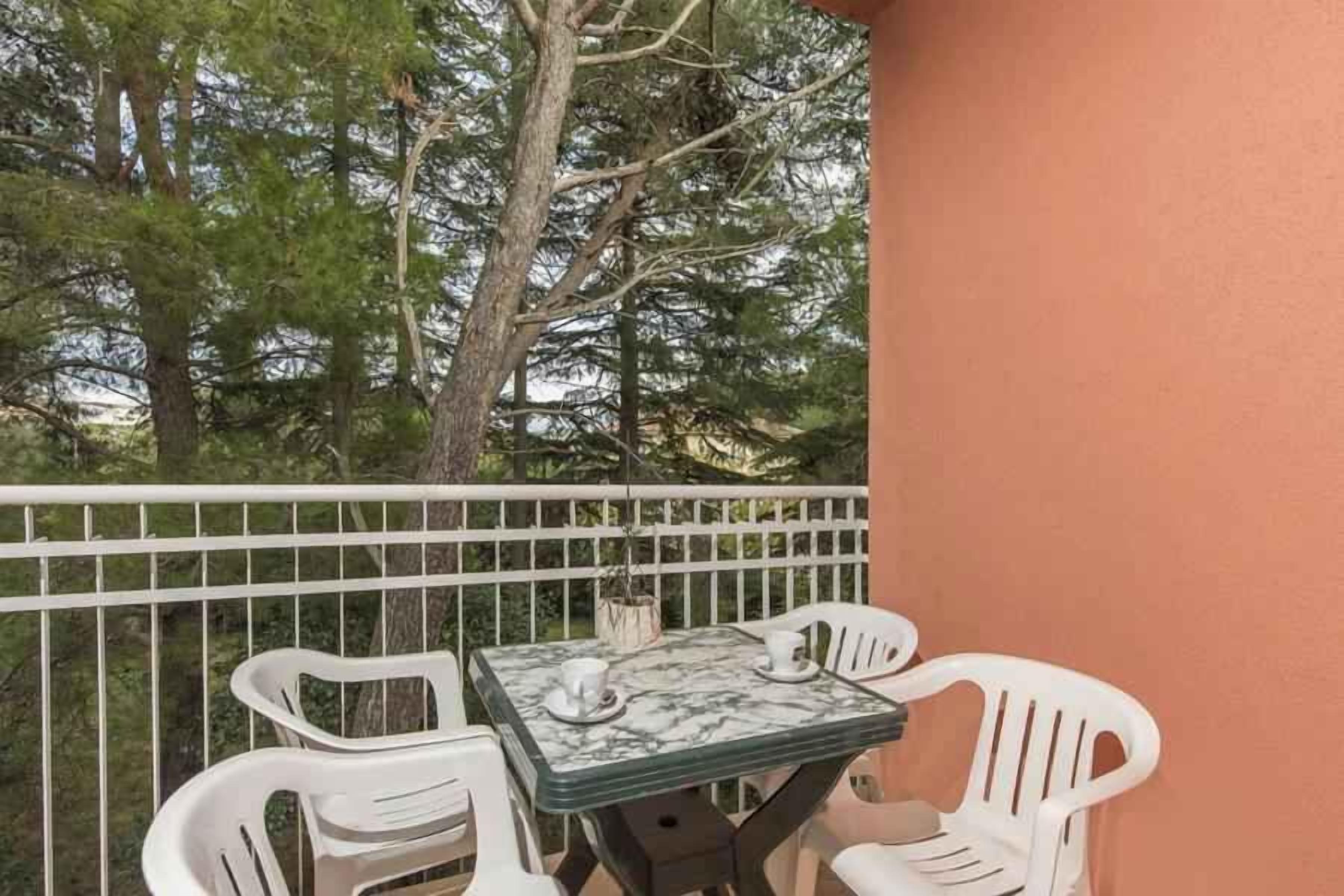 Un balcon avec une petite table et deux chaises blanches, entouré d’une balustrade blanche.