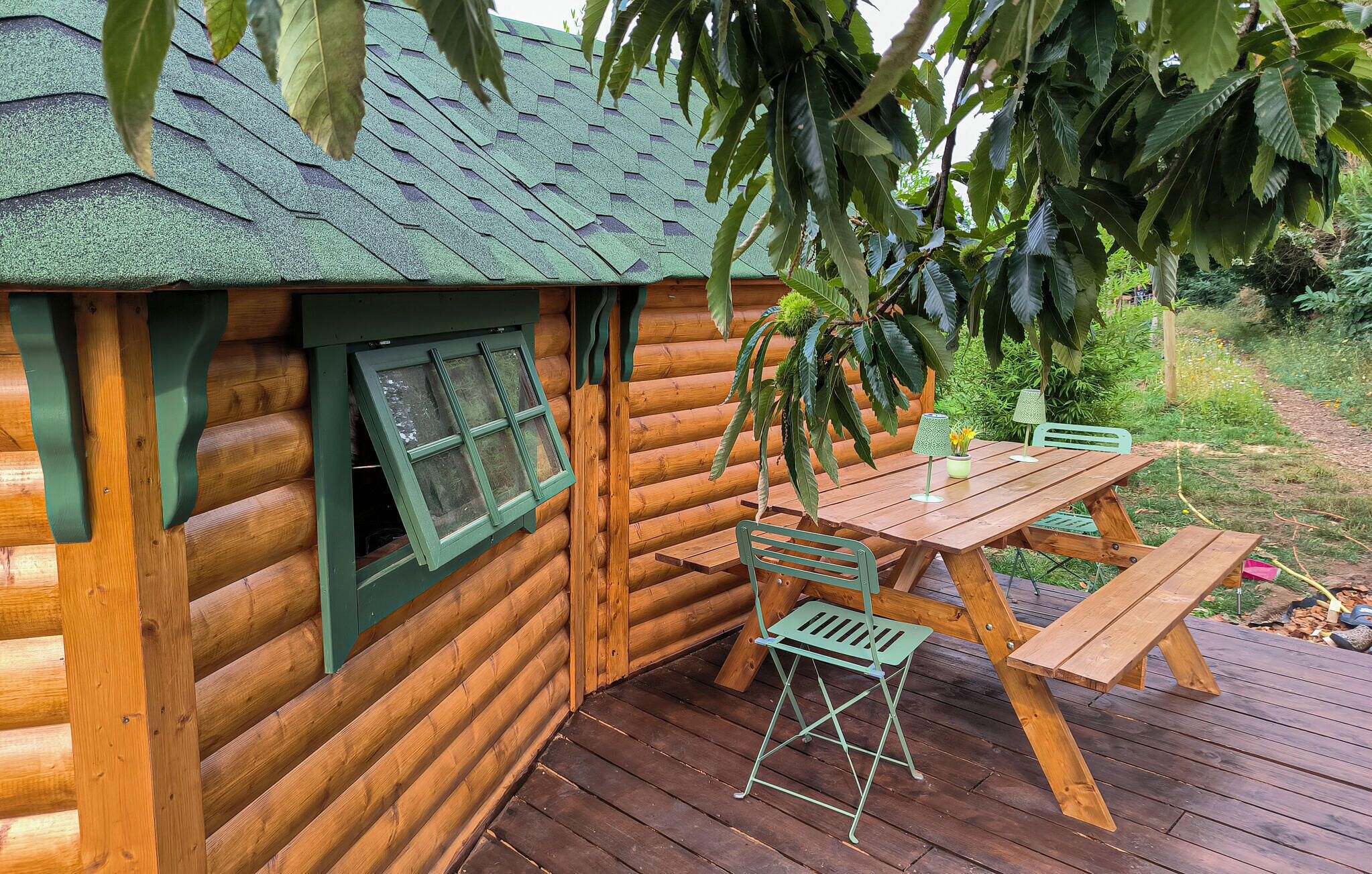 A wooden cabin with a green roof and a deck with a table and chairs.