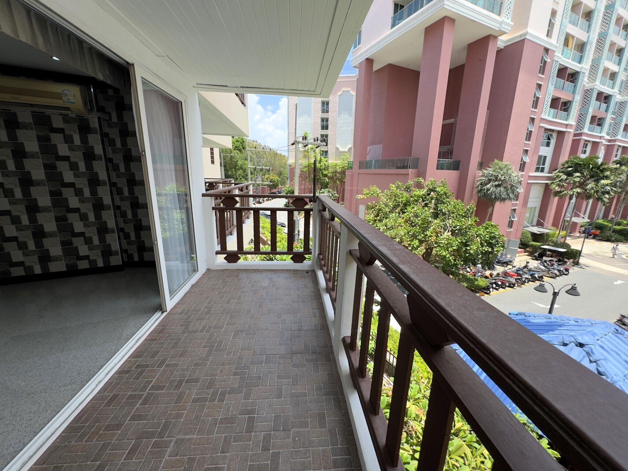 Un balcone con vista su una zona residenziale, caratterizzata da una fila di edifici rosa e motociclette parcheggiate.