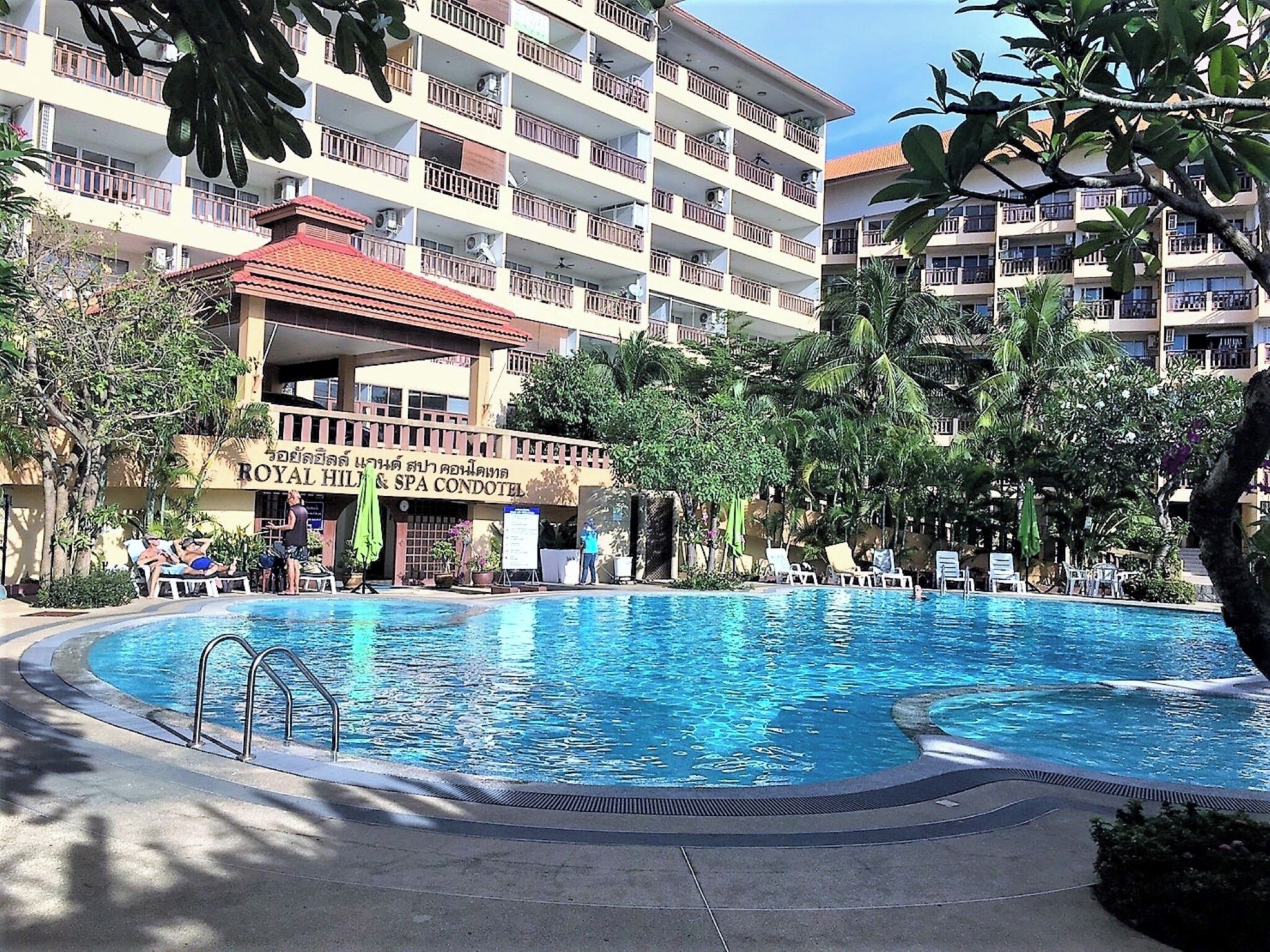 A hotel with a swimming pool surrounded by lounge chairs and palm trees.